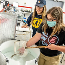 two women in a lab catching a fish with a net